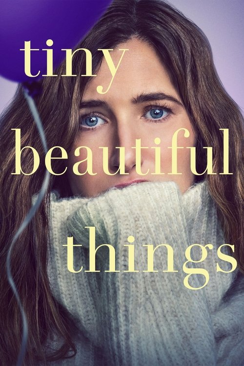 The poster features a woman with striking blue eyes and long brown hair, wearing a cozy gray sweater against a soft purple background. The title "tiny beautiful things" is elegantly written in a golden-yellow font, evoking warmth and charm. The overall mood is gentle and inviting, suggesting them...