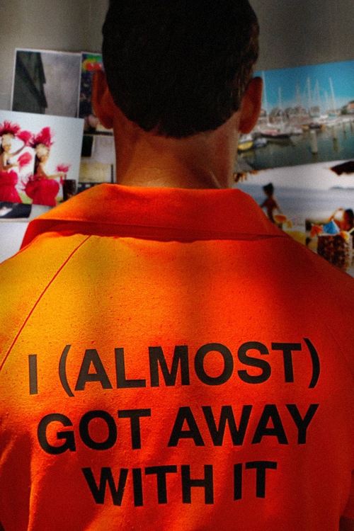 The poster features a person in an orange jumpsuit with bold text reading "I (ALMOST) GOT AWAY WITH IT." The background shows a blurred cityscape, suggesting urban exploration. The mood is mysterious and adventurous, hinting at a thrilling escape story.