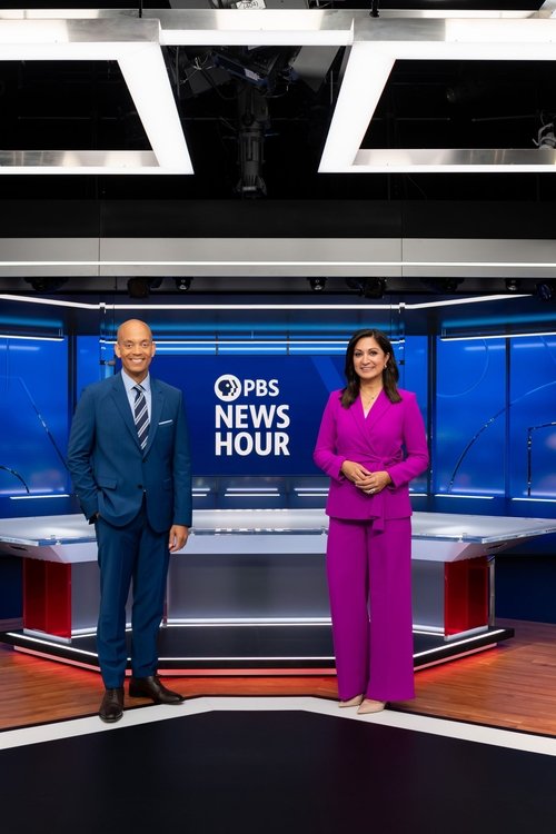 Two news anchors stand confidently in a vibrant studio, with one in a blue suit and the other in a striking purple ensemble. The backdrop features bold blue and white tones, emphasizing the show's professional yet energetic atmosphere.
