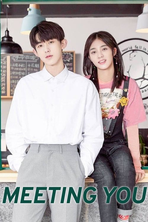 The poster features a young couple standing in a cozy, warmly lit room with soft lighting and a clock in the background. The man wears a crisp white shirt and gray pants, while the woman dons a pink top over a graphic tee and jeans. Their casual yet stylish attire suggests a relaxed, friendly atm...